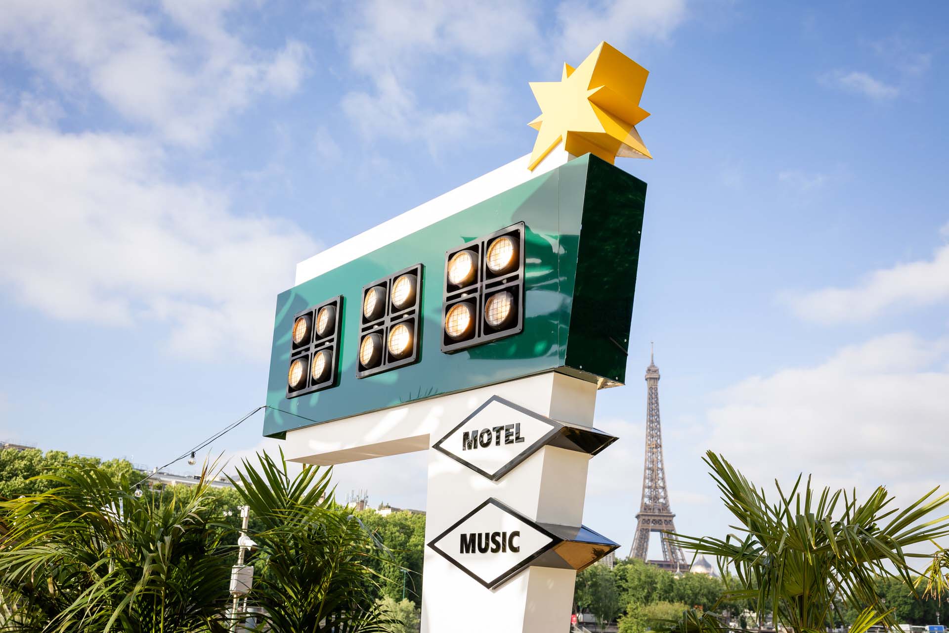 Enseigne rétro “Motel Music” sur le rooftop de Mademoiselle Mouche à Paris, entourée de palmiers avec la Tour Eiffel en arrière-plan, capturant l’atmosphère décalée et estivale du lieu.