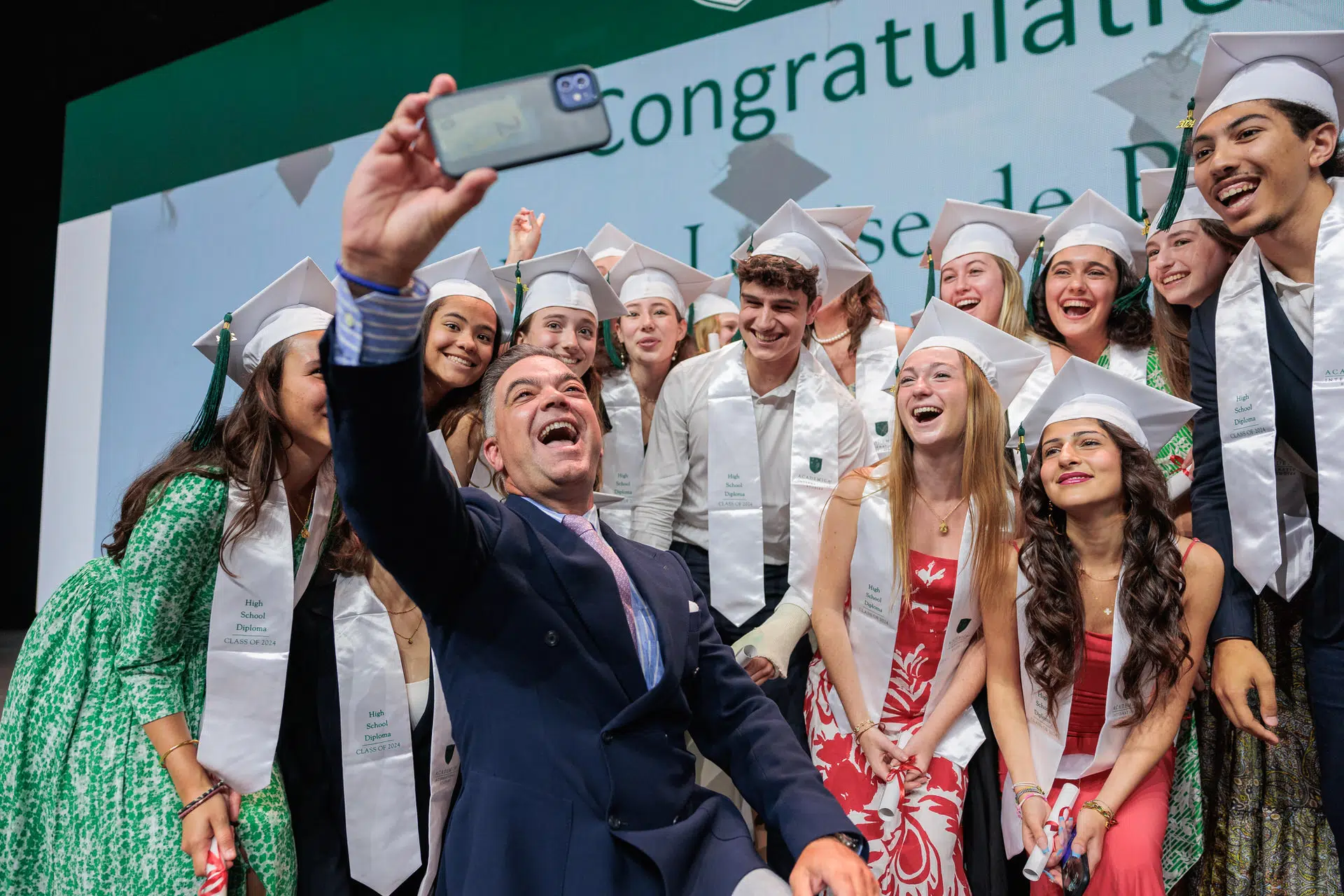 remise des diplômes 2024-dôme de paris-porte de Versailles-Academica Dual Diploma-306 A joyous moment captured on stage during a collective selfie of graduates in formal wear, gathered around their manager.