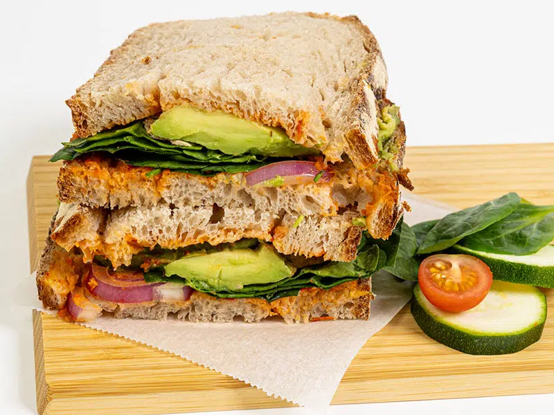 Food product shot of a whole-grain avocado sandwich on a wooden board — white-background studio food photography, Paris
